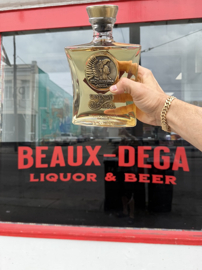 A bottle held in front of the Beaux-dega window lettering